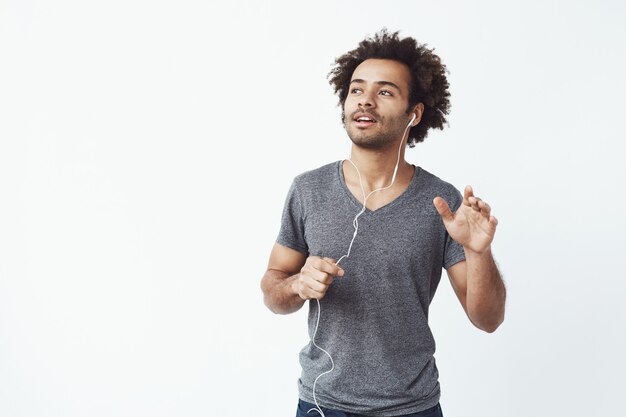 Hombre africano alegre escuchando música en auriculares bailando cantando.