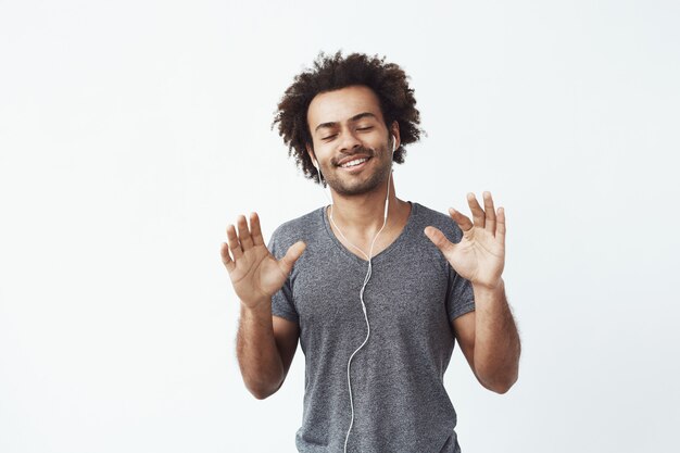 Hombre africano alegre escuchando música en auriculares bailando cantando.