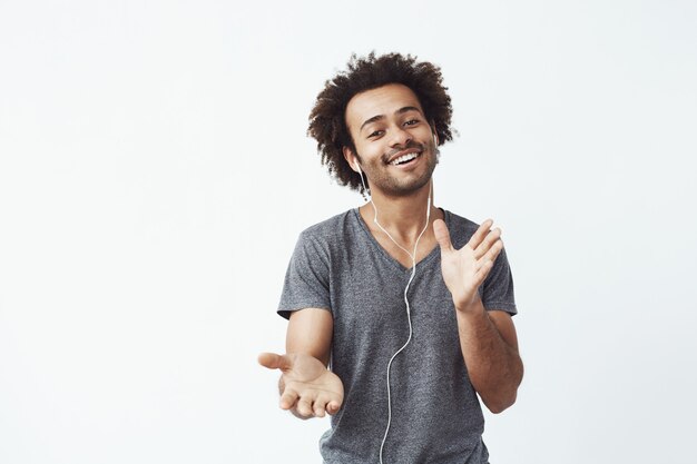 Hombre africano alegre escuchando música en auriculares bailando cantando.