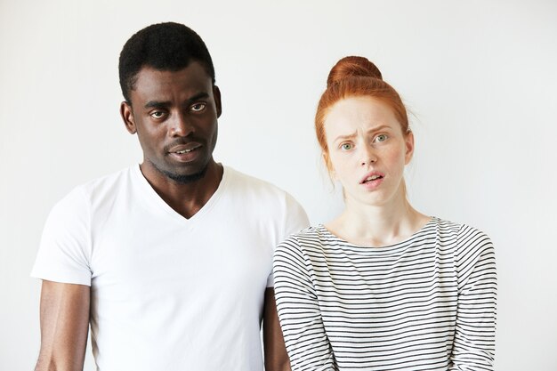 Hombre africano en camiseta blanca y mujer caucásica pelirroja en top rayado