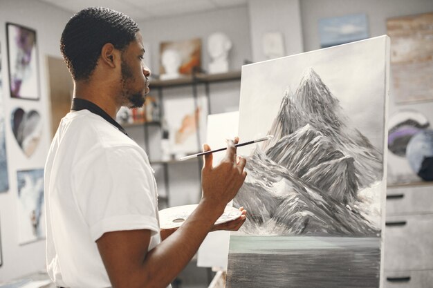 Hombre africano en clase de pintura dibujando sobre un caballete.