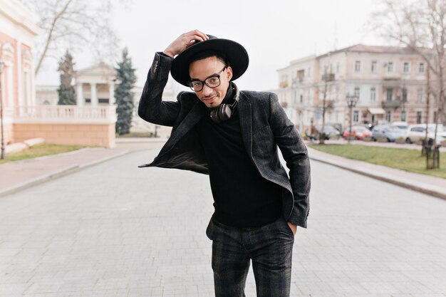 Hombre africano delgado soñador en traje a cuadros posando con placer en el parque. Retrato al aire libre del niño negro sonriente en traje elegante de pie