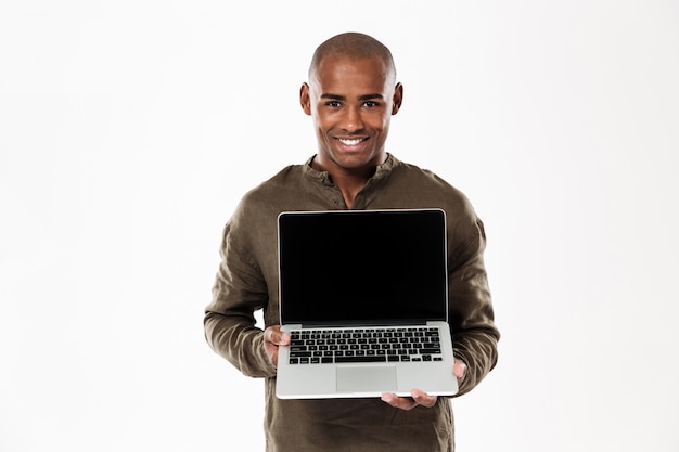 Hombre africano feliz que muestra la pantalla de la computadora portátil en blanco y mirando
