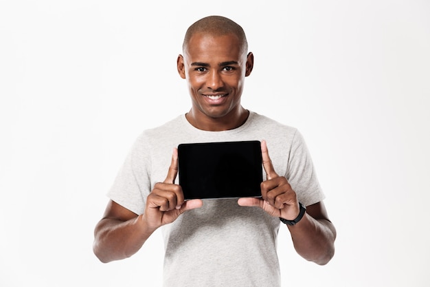 Hombre africano feliz que muestra la pantalla de la tableta en blanco y mirando