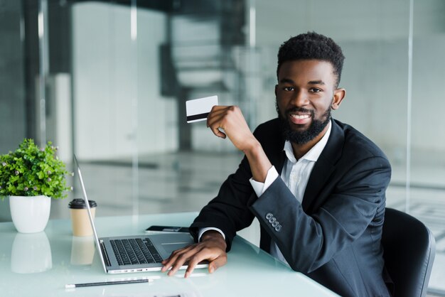 Hombre africano hablando por teléfono y leyendo el número de tarjeta de crédito mientras está sentado en la oficina