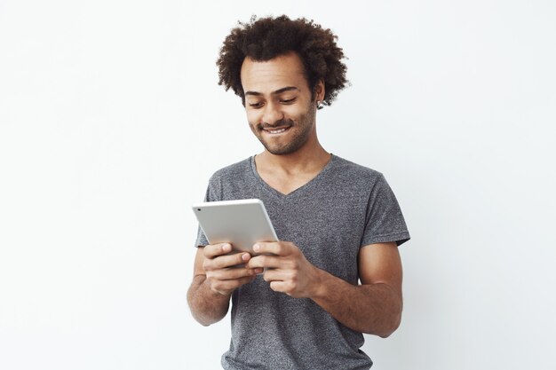 Hombre africano joven interesado y concentrado mirando tableta jugando un juego de plataformas y disfrutando de nuevos niveles sobre blanco filosófico.