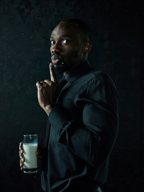 Hombre africano joven sano ahuecando la taza de leche en un estudio de bllack.