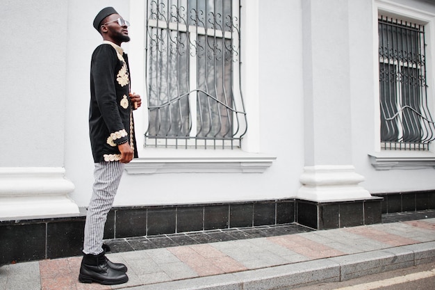 Hombre africano mega elegante en pose de chaqueta tradicional Chico negro de moda con sombrero y gafas de sol con cigarro en la mano