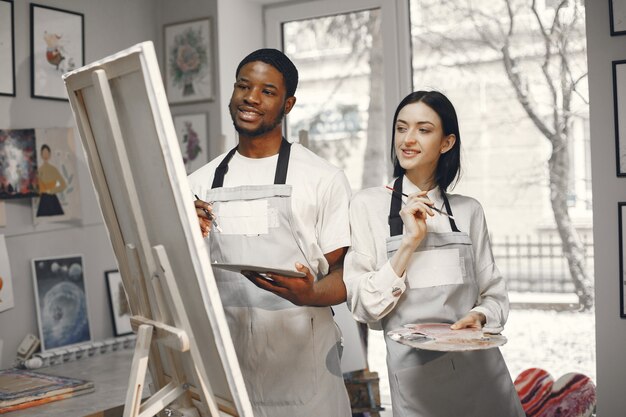 Hombre africano y una mujer en clase de pintura dibujando sobre un caballete.