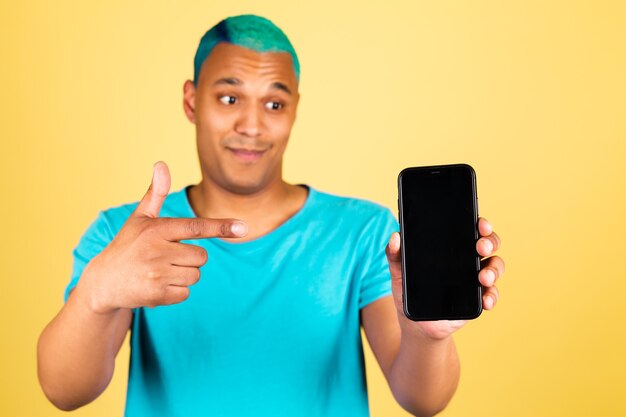 Hombre africano negro en casual en la pared amarilla con el dedo índice del punto feliz positivo del teléfono móvil en la pantalla vacía negra