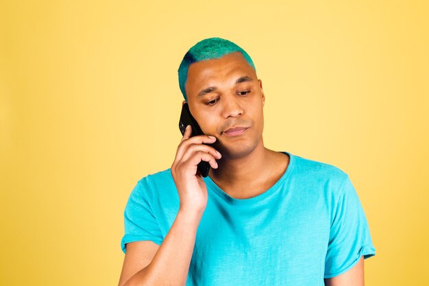 Hombre africano negro en casual en pared amarilla con teléfono móvil escucha voz con cara cansada aburrida