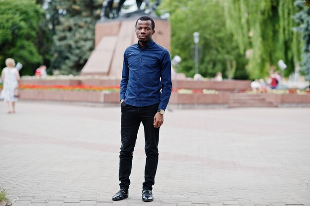 Hombre africano posó en la calle de la ciudad con camisa azul y pantalones negros