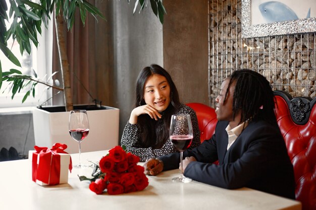 Hombre africano con rastas. Vasos con vino tinto. Abrazos de una pareja enamorada.