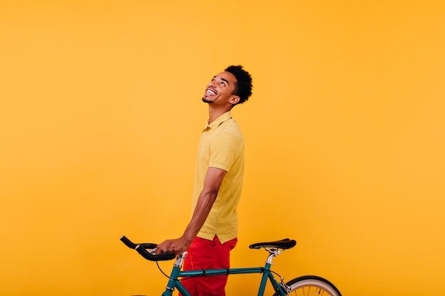 Foto gratuita hombre africano refinado mirando hacia arriba con bicicleta. foto interior de chico negro despreocupado divirtiéndose.