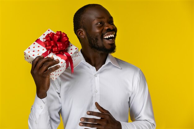 Hombre africano sonriente mirando a otro lado y sosteniendo una caja de regalo