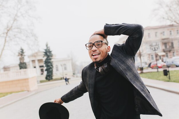 Hombre africano sorprendido en vasos grandes posando emocionalmente en el parque. Chico negro entusiasta en chaqueta gris a cuadros de pie en la ciudad.