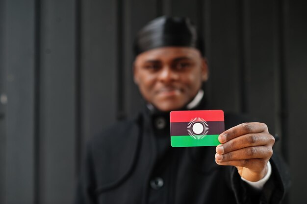 El hombre africano usa durag negro y sostiene la bandera de Malawi en un fondo oscuro aislado a mano