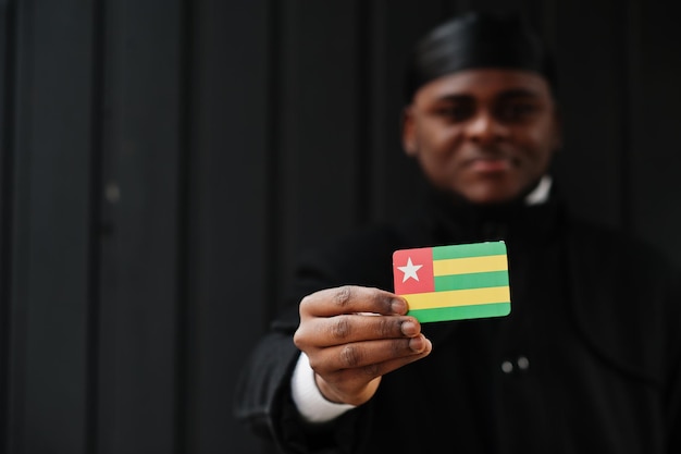 El hombre africano usa durag negro y sostiene la bandera de Togo en un fondo oscuro aislado a mano