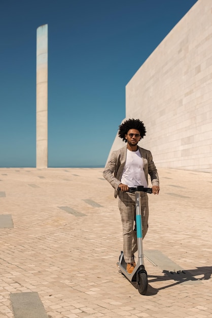 Hombre afroamericano activo montando scooter eléctrico. Hombre con cabello rizado con gafas de sol pasando tiempo al aire libre. Tecnología, concepto de actividad