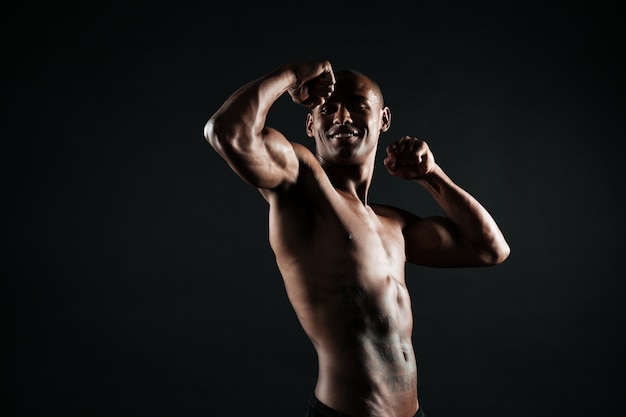 Hombre afroamericano alegre de los deportes que muestra sus bíceps