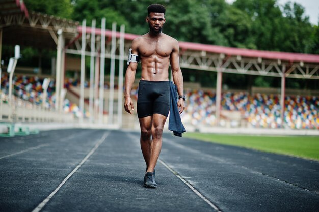 Hombre afroamericano atleta sexy deporte torso desnudo hombre con funda de brazo deportivo para teléfono móvil posado en el estadio