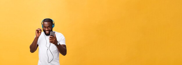 Hombre afroamericano con auriculares escucha y baila con música aislada de fondo amarillo