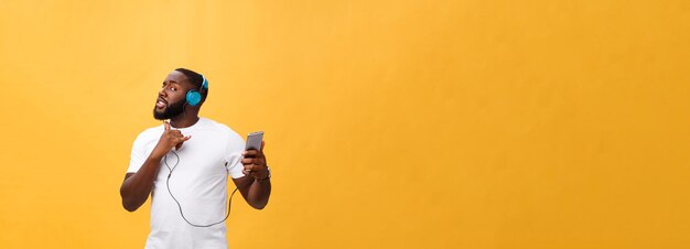 Hombre afroamericano con auriculares escucha y baila con música aislada de fondo amarillo