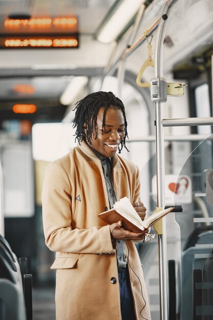 Hombre afroamericano en el autobús de la ciudad. Chico con un abrigo marrón. Hombre con cuaderno.