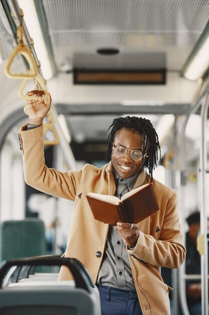 Hombre afroamericano en el autobús de la ciudad. Chico con un abrigo marrón. Hombre con cuaderno.