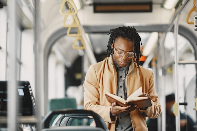 Hombre afroamericano en el autobús de la ciudad. Chico con un abrigo marrón. Hombre con cuaderno.