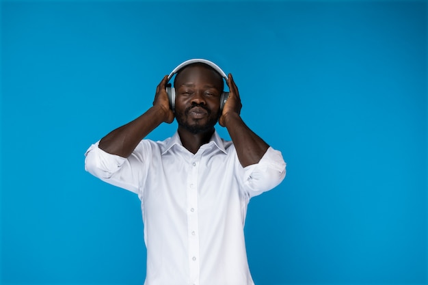 Hombre afroamericano barbudo con los ojos cerrados está en grandes auriculares con camisa blanca