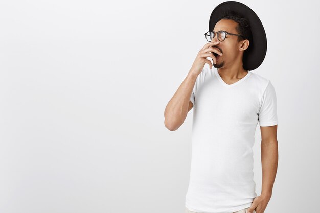 Hombre afroamericano cansado o soñoliento en camiseta casual bostezando, tapando la boca abierta con la mano, sintiéndose agotado