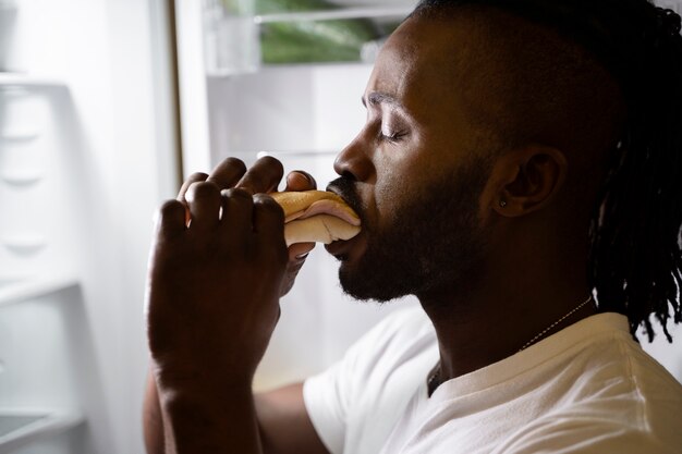 Hombre afroamericano comiendo de la nevera por la noche