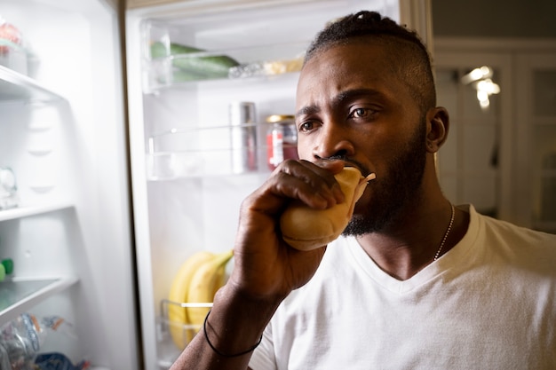 Hombre afroamericano comiendo de la nevera por la noche