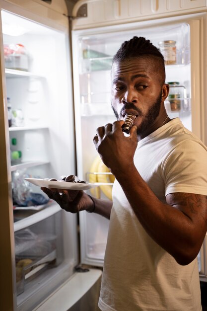 Hombre afroamericano comiendo de la nevera por la noche
