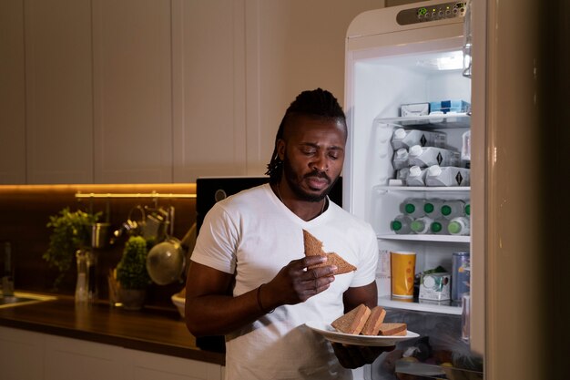 Hombre afroamericano comiendo de la nevera por la noche