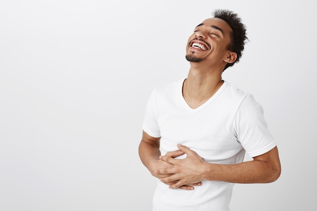 Hombre afroamericano despreocupado riendo y sonriendo, escucha una broma divertida