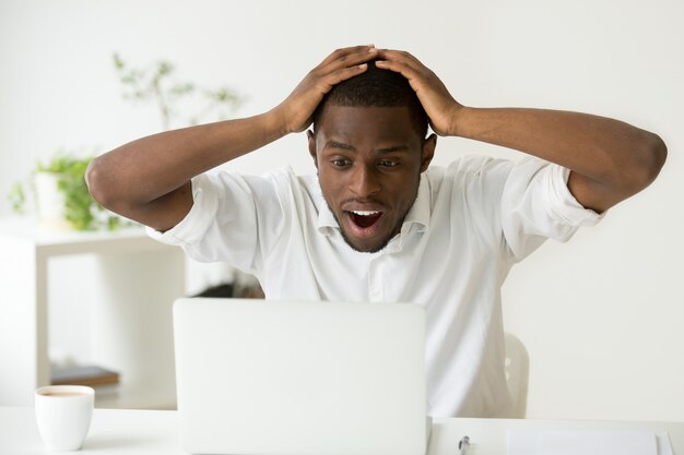 Hombre afroamericano emocionado asombrado sorprendido por inesperadas buenas noticias en línea