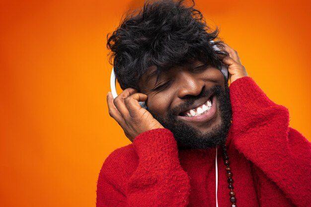 Hombre afroamericano escuchando música con alegría sobre fondo naranja