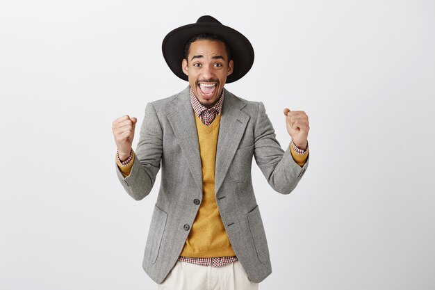 Hombre afroamericano ganador exitoso en traje celebrando la victoria, sonriendo emocionado y bomba de puño en regocijo