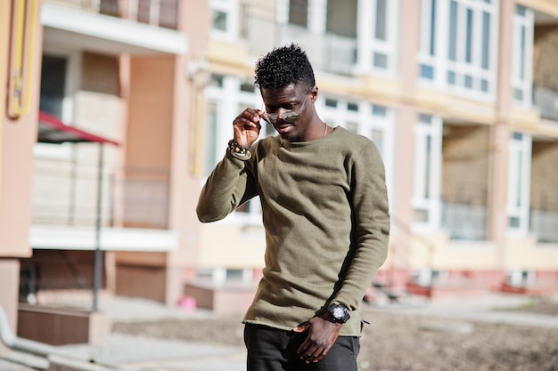 Hombre afroamericano guapo y atractivo con gafas de sol posando junto al edificio alto en una calle