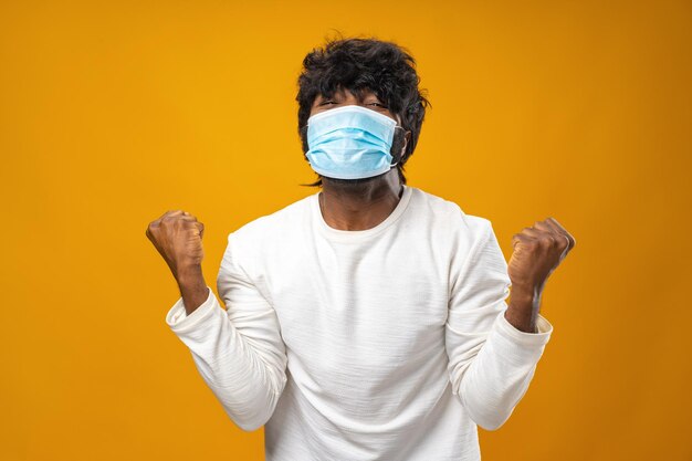 Hombre afroamericano guapo positivo con máscara médica contra el fondo amarillo