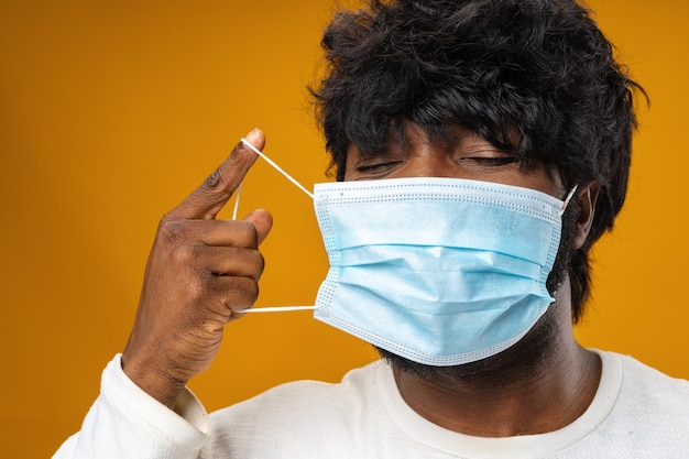 Hombre afroamericano guapo positivo con máscara médica contra el fondo amarillo