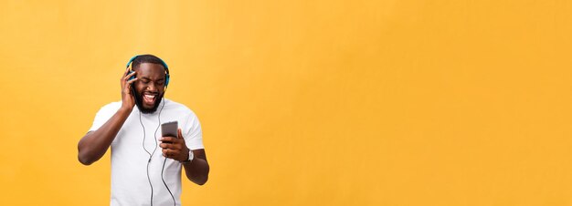 Hombre afroamericano joven con auriculares y disfrutar de la música sobre fondo de oro amarillo