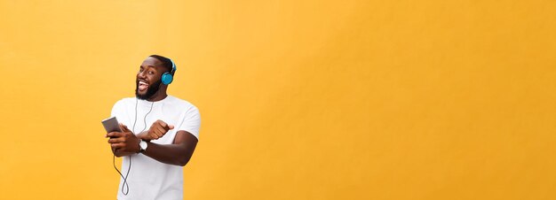 Hombre afroamericano joven con auriculares y disfrutar de la música sobre fondo de oro amarillo