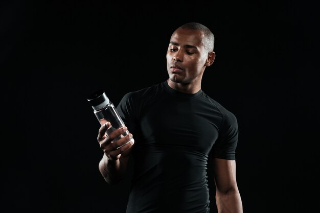 Hombre afroamericano joven de los deportes que sostiene la botella de agua