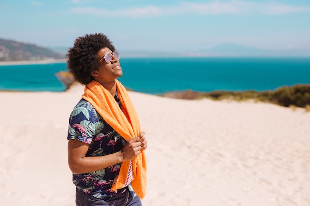 Foto gratuita hombre afroamericano joven satisfecho que se coloca en la playa