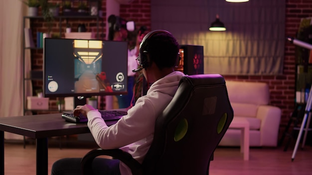 Hombre afroamericano jugando rpg de acción en línea multijugador en pc mientras su novia está peleando en un juego de realidad virtual en la sala de estar. Gamer transmitiendo tirador en primera persona mientras la mujer usa gafas vr.