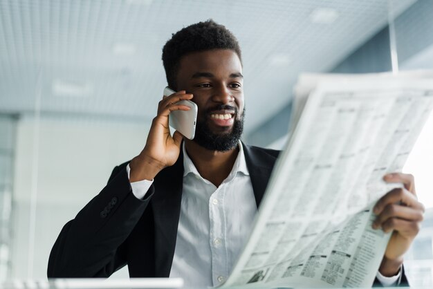 Hombre afroamericano leyendo el periódico y hablando por teléfono en la oficina