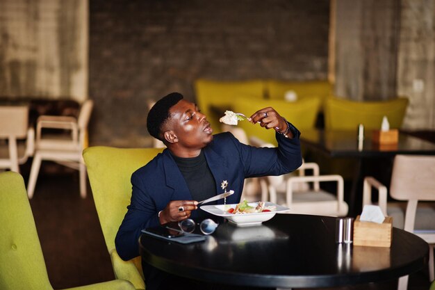 Hombre afroamericano de moda en traje sentado en el café y comiendo ensalada